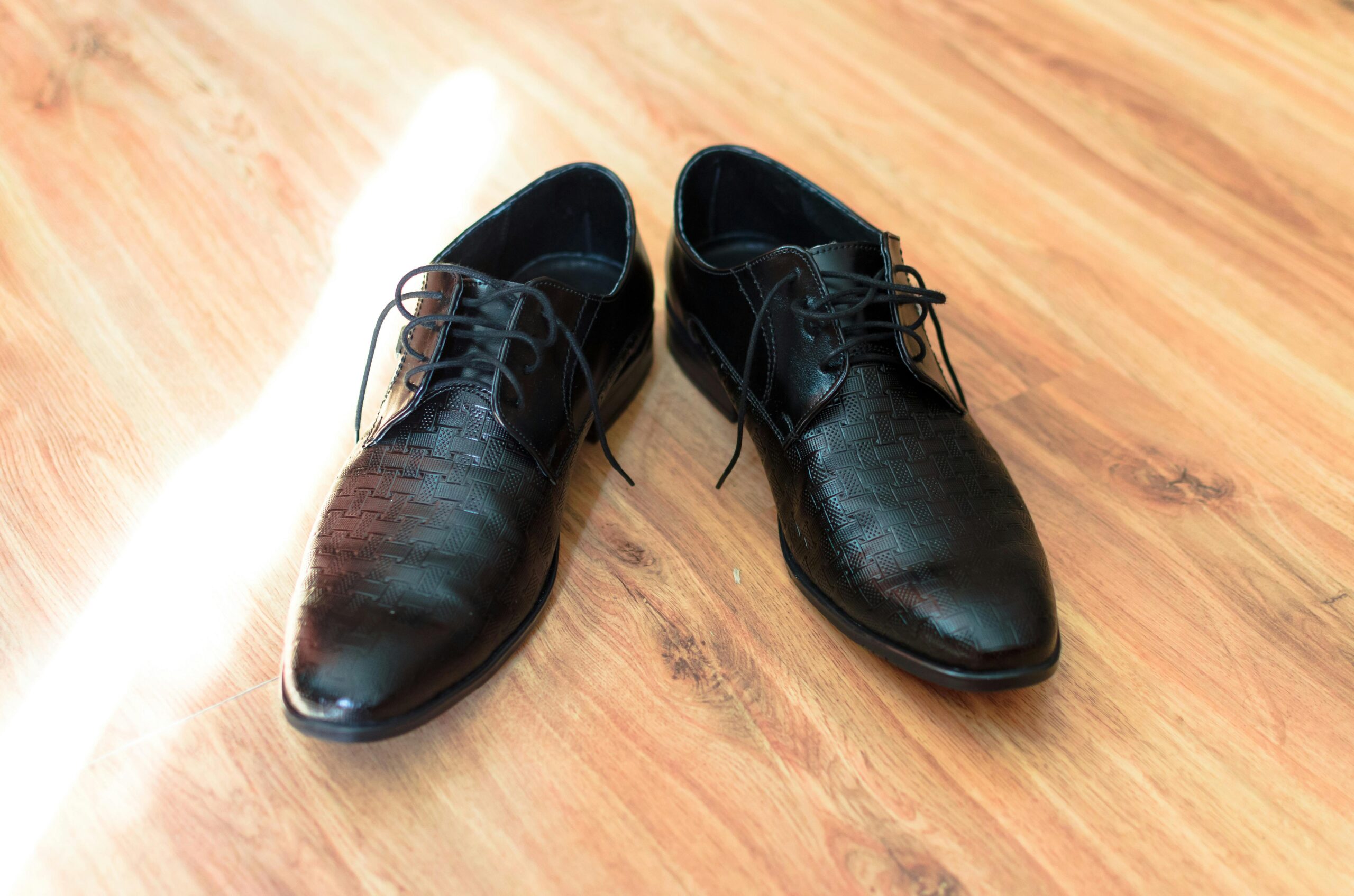 A pair of stylish black leather dress shoes with laces on a wooden floor, highlighting their elegance and design.